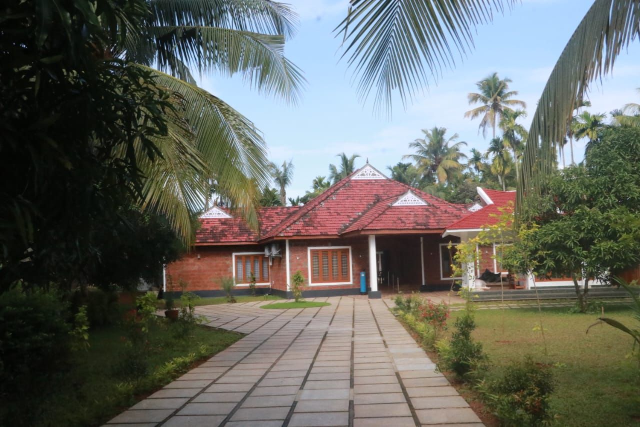 Kumarakom Nest main house with a stone-paved walkway and coconut palms